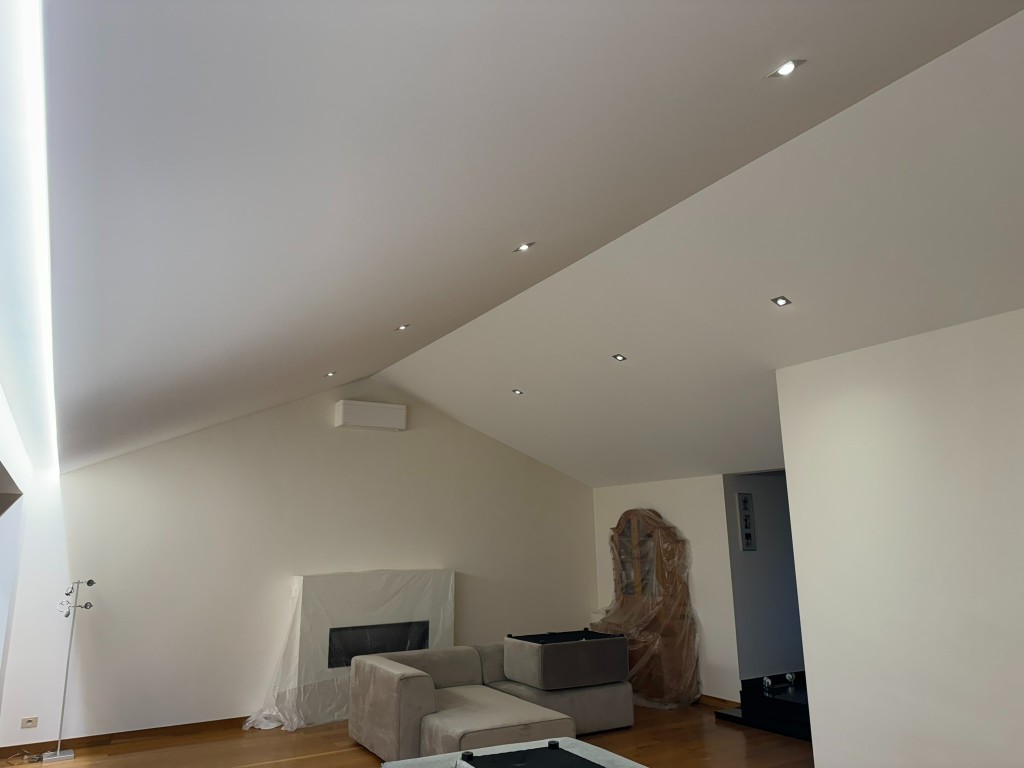 Strak wit schuin plafond met inbouwspots en lijnverlichting in een lichte woonruimte
